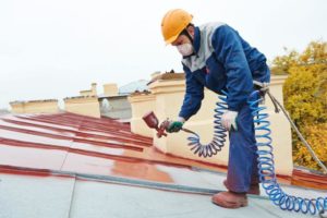 Professional roofers spraying paint on a metal roof for a fresh, durable finish.