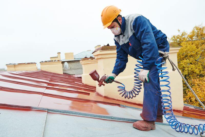 Professional roofers spraying paint on a metal roof for a fresh, durable finish.
