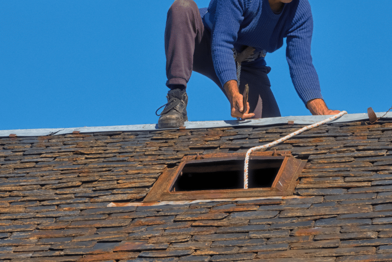 Man working on natural slate roof repair on a residential roof