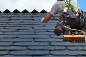 Worker doing natural slate roof repair on damaged slate tiles