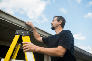 Roof leak inspection process with roofer inspecting roof edge on ladder